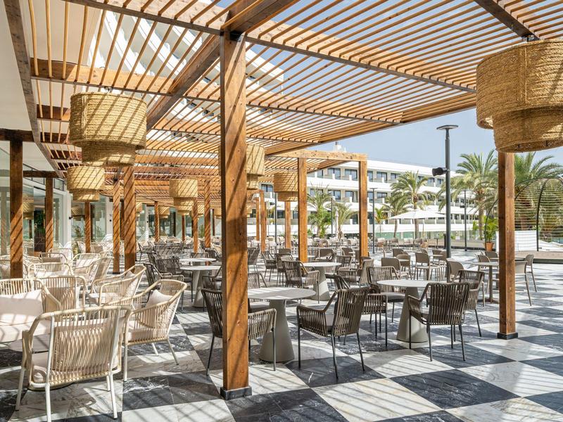 Espace repas ouvert avec mobilier en bois et abat-jour tissés dans un lieu de vacances ensoleillé.