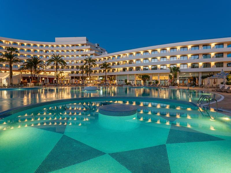 Hôtel moderne avec piscine éclairée et ciel nocturne clair.