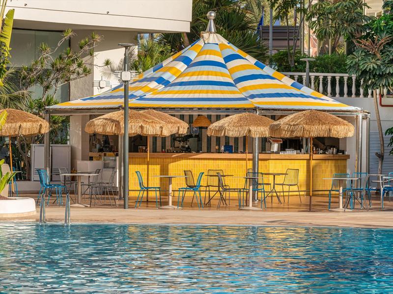 Parasol coloré et bar à côté d'une piscine avec chaises et parasols.