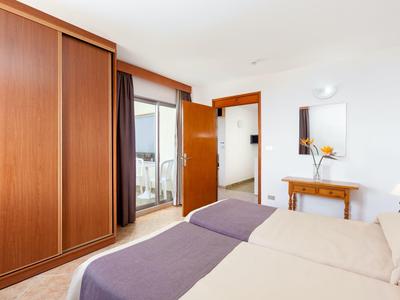 Hell eingerichtetes Schlafzimmer mit Holzmöbeln, Doppelbett und Zugang zum Balkon.