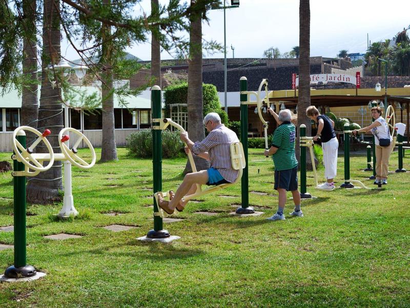 Mehrere Personen nutzen im Park draußen verschiedene Fitnessgeräte bei Tageslicht.