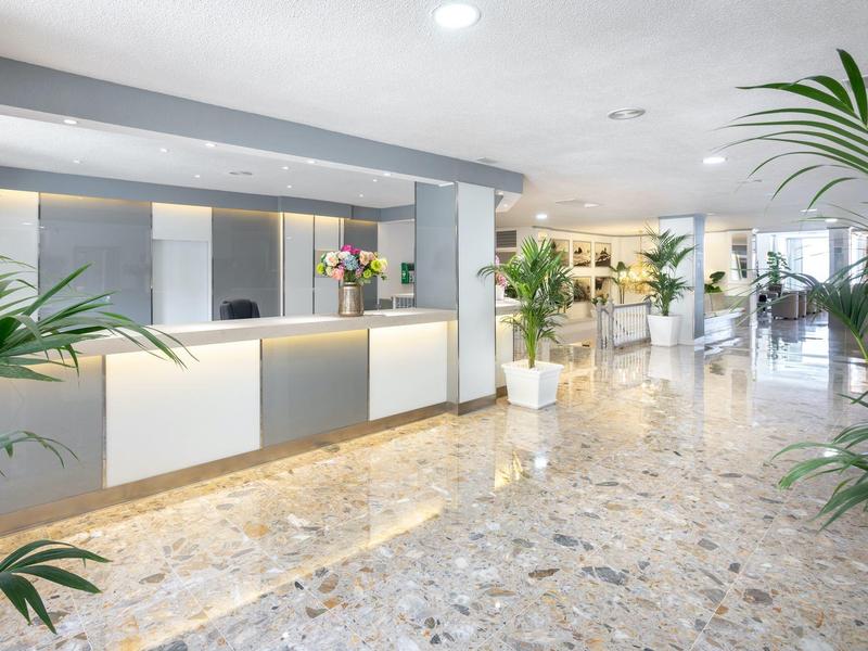 Heller Empfangsbereich mit Marmorfliesen, Theke, Blumendekor und grünen Pflanzen.