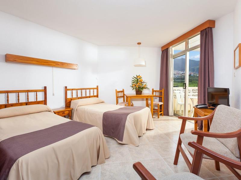 Helles Schlafzimmer mit zwei Einzelbetten, Holzmöbeln und Balkon mit Bergblick.
