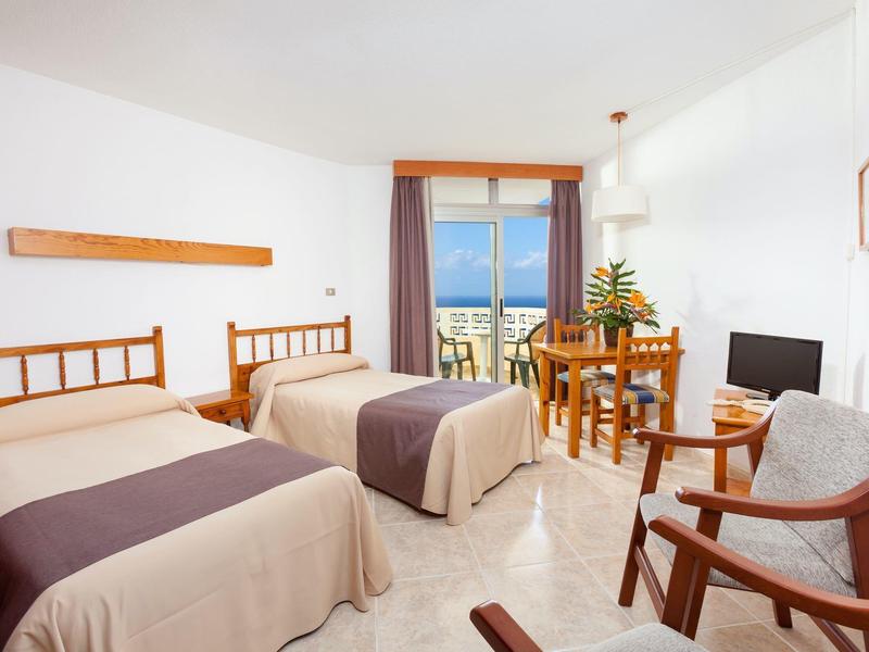 Hell eingerichtetes Zimmer mit zwei Einzelbetten, Holzmöbeln und Balkon mit Meerblick.