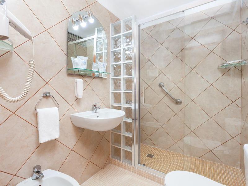 Helles Badezimmer mit Waschtisch, Spiegel, Dusche mit Glaswand und weißen Fliesen an den Wänden.