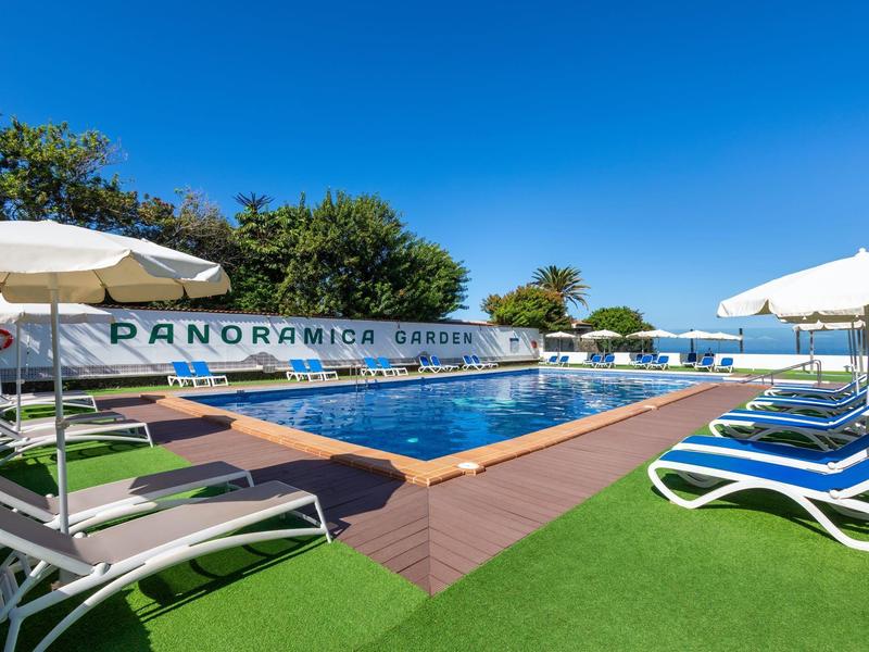 Schwimmbad mit blauer Wasserfläche, Sonnenliegen, weißen Schirmen und klarem blauem Himmel.