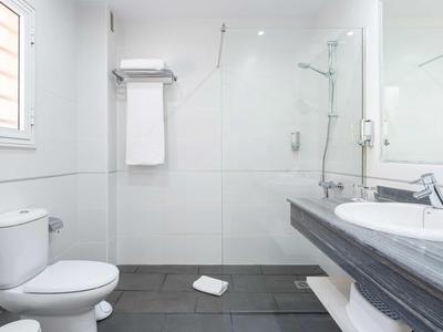 Salle de bain d'hôtel moderne avec douche, lavabo, toilettes et serviettes blanches.