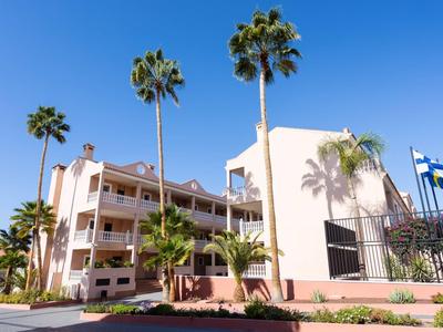 Bâtiment d'hôtel moderne avec grands palmiers et ciel bleu clair en arrière-plan.