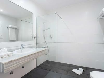 Salle de bain moderne blanche avec grande douche en verre et carrelage gris.