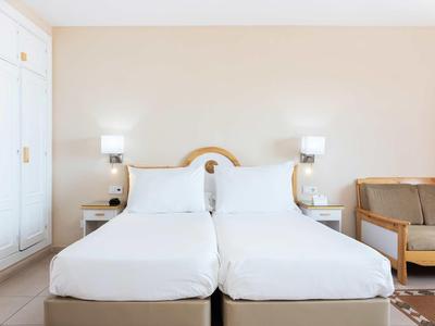 Deux lits simples aux draps blancs dans une chambre d'hôtel moderne avec canapé et lampes.