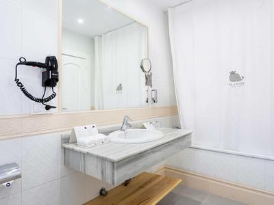 Salle de bain d'hôtel moderne avec grand miroir, lavabo et sèche-cheveux mural.