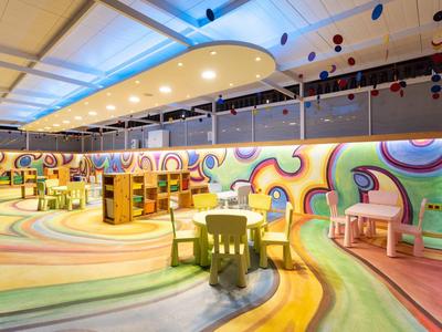 Espace de jeu coloré et moderne pour enfants dans un hôtel avec tables et chaises.