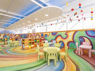 Salle de jeux colorée pour enfants avec tables, chaises et fresques murales joyeuses.