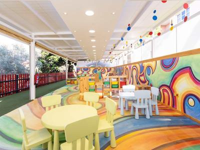 Espace de jeu intérieur coloré pour enfants avec tables, chaises et toboggan dans une ambiance lumineuse