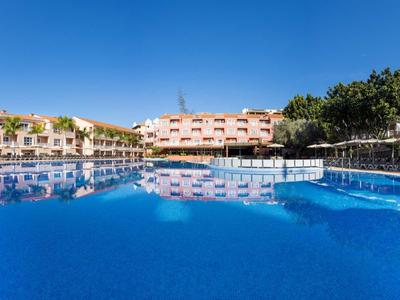 Large outdoor swimming pool in front of multi-story residential buildings under clear sky.