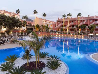 Large pool with palm trees and hotel buildings in the background at evening lighting.