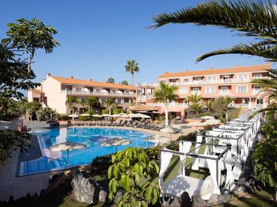 Hotel with pool, sun loungers, and palm trees under a clear blue sky.