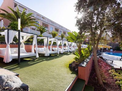 Lits blancs luxueux avec coussins roses à côté d'une piscine dans un complexe hôtelier.