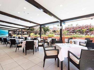 Espace de restaurant d'hôtel ouvert avec des tables dressées et des chaises noires sous un toit couvert.