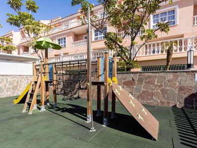 Aire de jeux moderne avec toboggan et filet d'escalade devant un immeuble résidentiel.