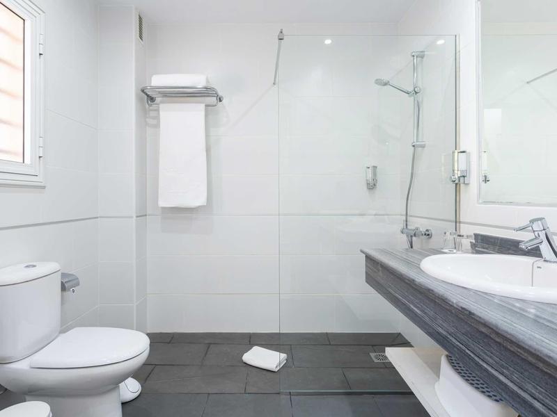 Salle de bain d'hôtel moderne avec douche, lavabo, toilettes et serviettes blanches.