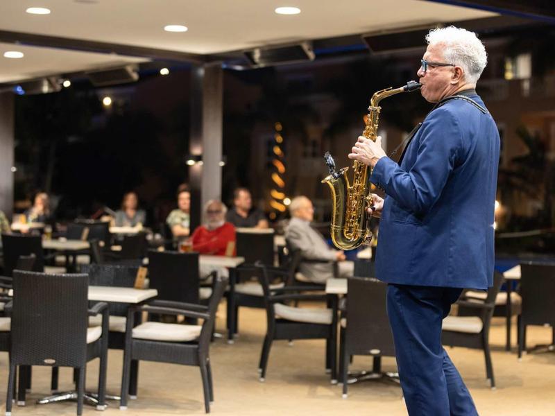 Un homme plus âgé joue du saxophone devant un public assis dans un restaurant ou une salle d'événements.