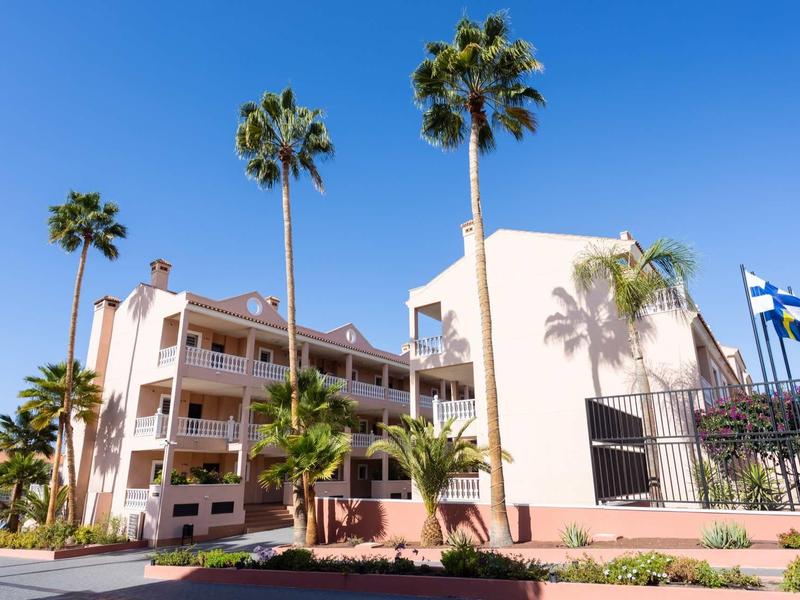 Bâtiment d'hôtel moderne avec grands palmiers et ciel bleu clair en arrière-plan.