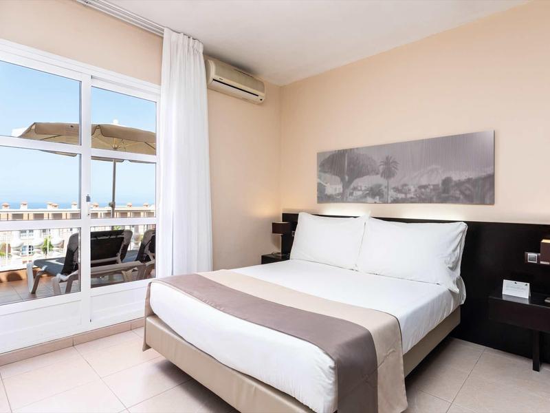 Chambre d'hôtel lumineuse avec grand lit et vue sur une terrasse et la mer.