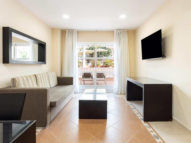 Chambre d'hôtel moderne avec canapé, TV murale et balcon donnant sur la cour.