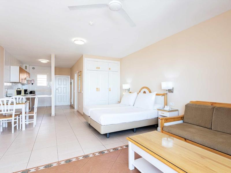 Chambre d'hôtel lumineuse avec lit double, canapé, table à manger et coin cuisine.