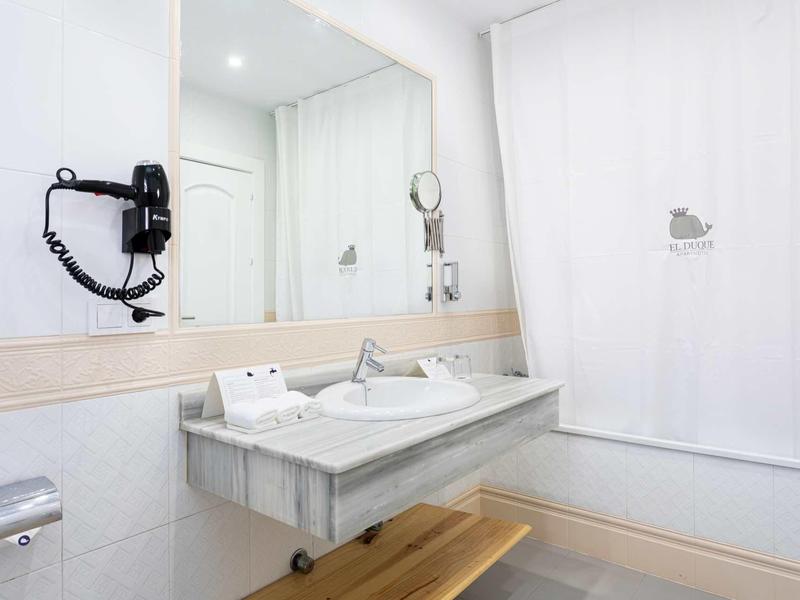 Salle de bain d'hôtel moderne avec grand miroir, lavabo et sèche-cheveux mural.