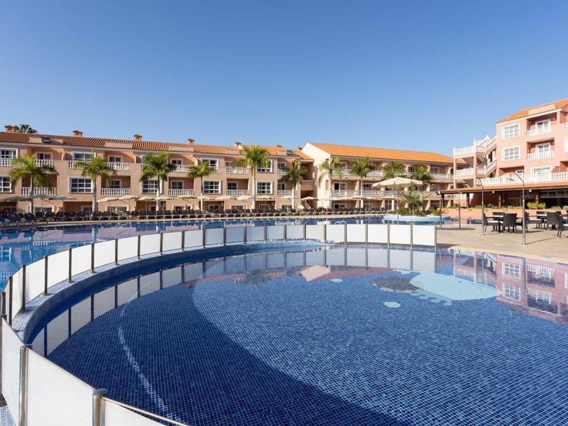 Grande piscine avec barrière et bâtiments d'hôtel en arrière-plan sous un ciel ensoleillé