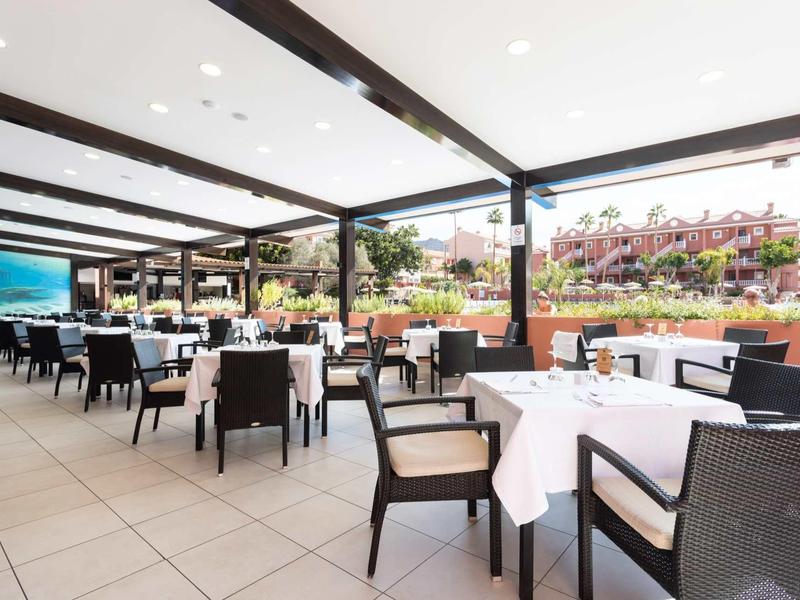 Espace de restaurant d'hôtel ouvert avec des tables dressées et des chaises noires sous un toit couvert.