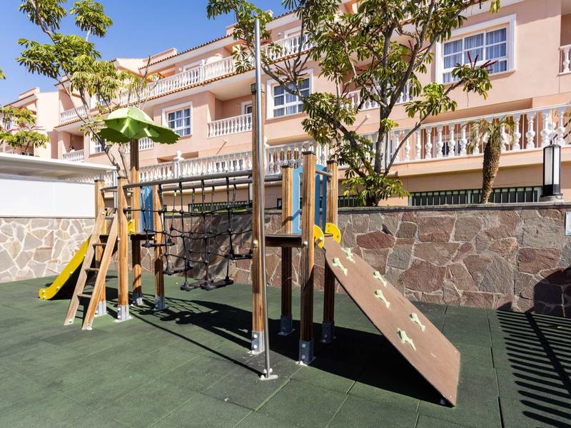 Aire de jeux moderne avec toboggan et filet d'escalade devant un immeuble résidentiel.