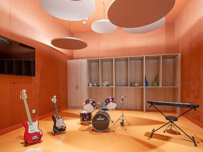 Musikraum mit Schlagzeug, Gitarren, Keyboard, orangefarbenen Wänden und abgerundeten Deckenelementen.
