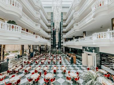 Großer heller Innenraum mit Marmorboden, weißen Geländern, roten Stühlen und zwei Aufzügen.