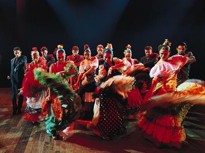 Kleurrijke flamencodansers in traditionele kleding op een houten podium.