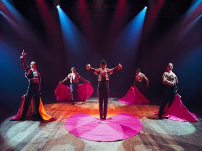 Vijf flamencodansers in traditionele kleding met felrode rokken op een podium met dramatische verlichting.
