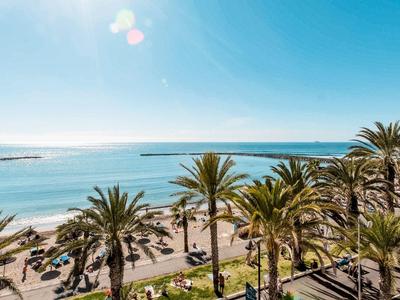Strand mit Palmen, Sonnenliegen und klar blauem Meer unter hellem Himmel.