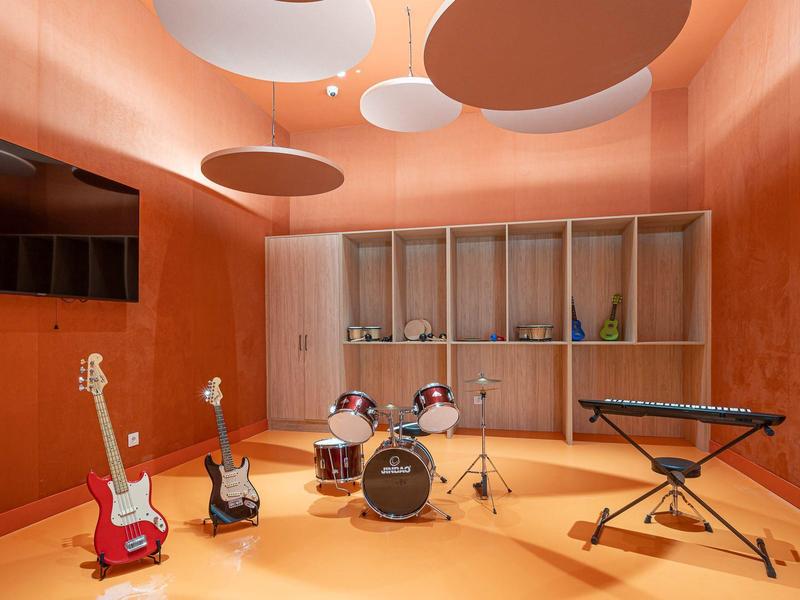Musikraum mit Schlagzeug, Gitarren, Keyboard, orangefarbenen Wänden und abgerundeten Deckenelementen.