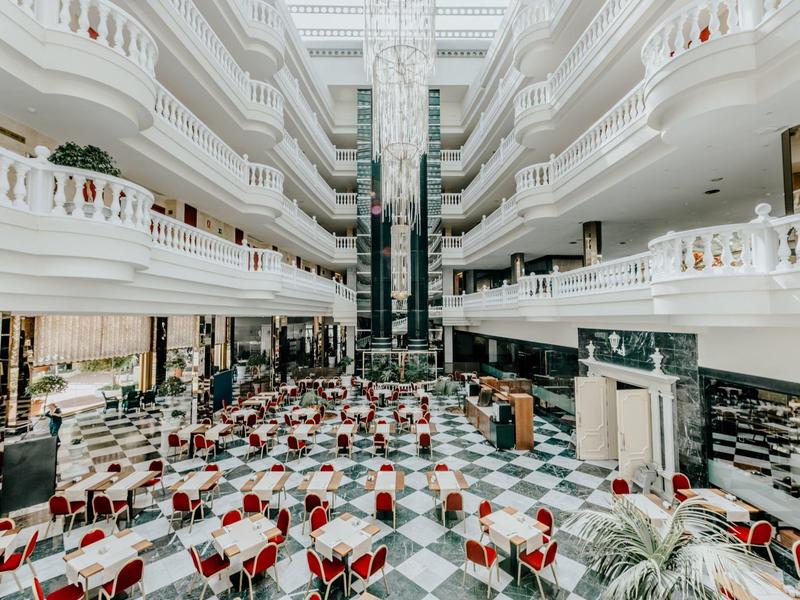 Großer heller Innenraum mit Marmorboden, weißen Geländern, roten Stühlen und zwei Aufzügen.