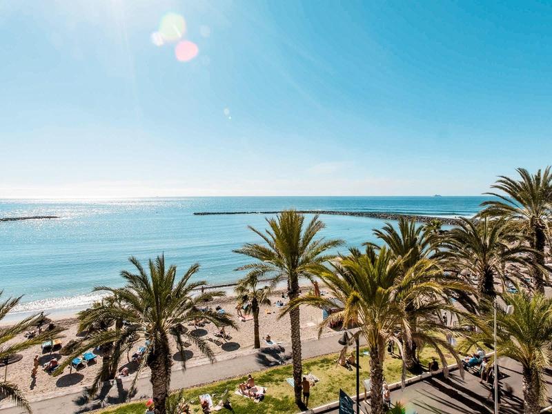 Strand mit Palmen, Sonnenliegen und klar blauem Meer unter hellem Himmel.