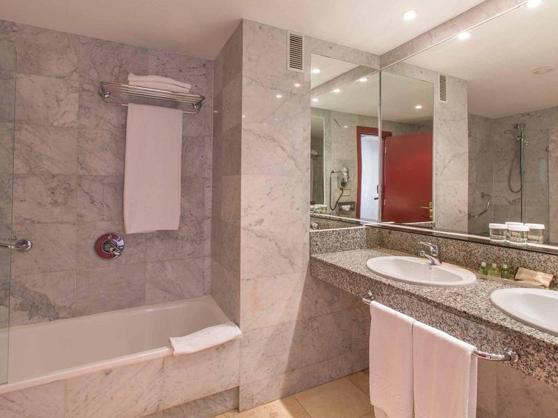 Helles Badezimmer mit grauen Marmorwänden, Badewanne, Doppelwaschbecken und großem Spiegel.