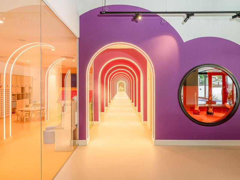 Heller Gang mit lila Wand, runden Spiegeln und pink-orangen Lichtbögen, moderne Innenraumgestaltung.