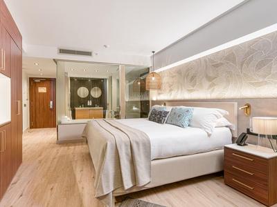 Modern hotelkamer met groot bed, houten vloer en glazen badkamer.