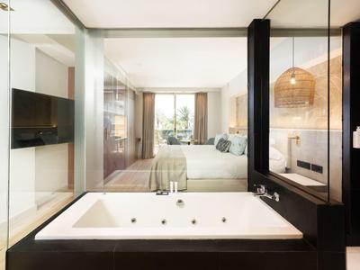 Moderne hotel suite met groot bad, slaapkamer en tv in lichte, elegante stijl.