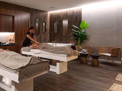 Moderne massageruimte met twee tafels, houten vloer en ontspannen sfeer.