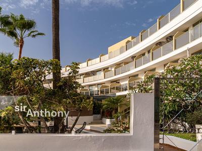 Modern hotelgebouw met palmbomen en tuin ervoor onder een heldere lucht.