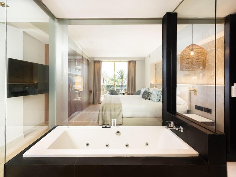 Moderne hotel suite met groot bad, slaapkamer en tv in lichte, elegante stijl.