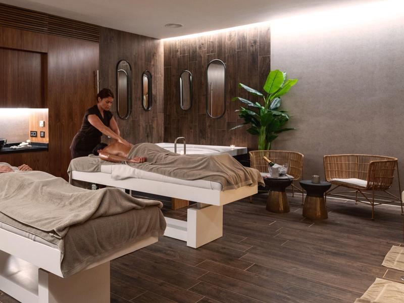 Moderne massageruimte met twee tafels, houten vloer en ontspannen sfeer.